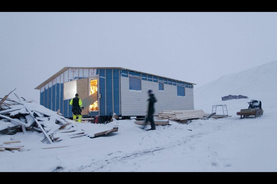 Einar Jenssen (t.v.) får hjelp til å bære inn plater til gulvet i hytta. Nesten alt av den gamle hytta som ble tatt av skred i fjor sommer er revet og bygget opp igjen.