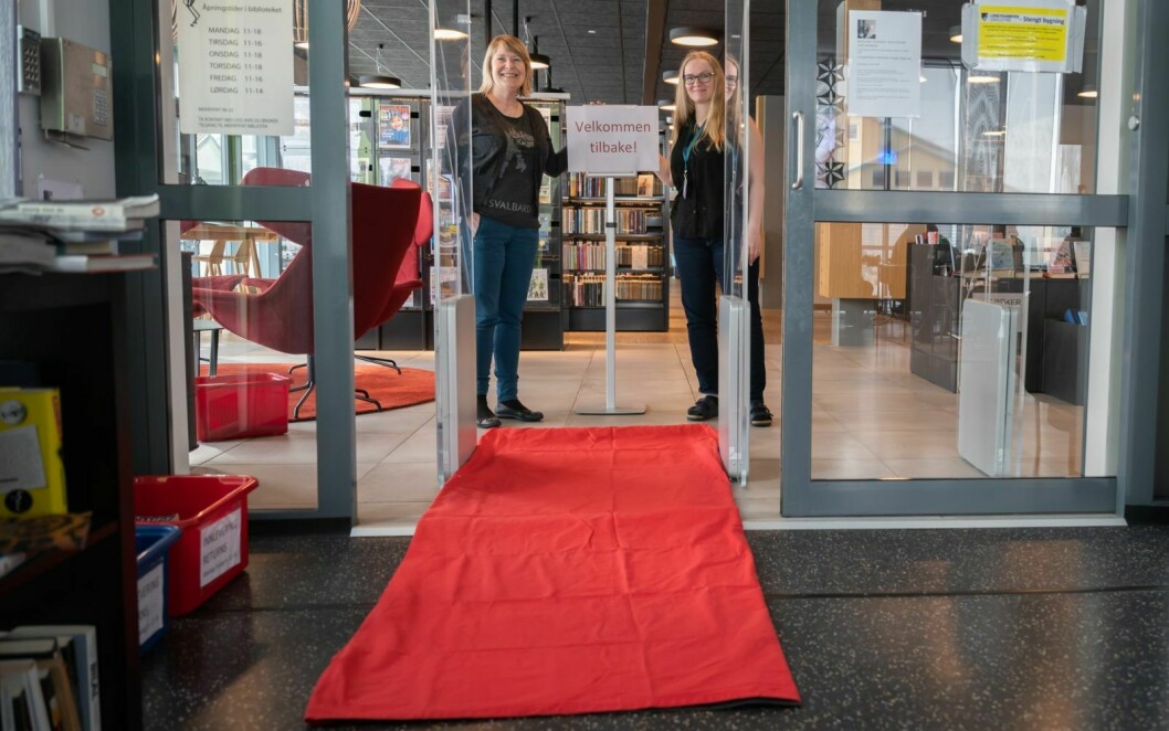 Biblioteksjef Elin Anita Olsrud (t.v.) og barne- og ungdomsbibliotekar Marie Mæland er glade for at de fra 18. mai kan åpne lokalene igjen. Med hjemmesnekra rød løper for anledningen.