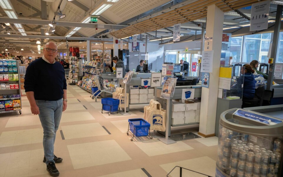 Svalbardbutikken, her ved daglig leder Ronny Strømnes, har innført mange smitteverntiltak. Blant annet sorte teip-streker for å skille avstanden i køen, plakater om avstand over kassene, og pleksiglass i kassene som står mellom de ansatte og kunden.
