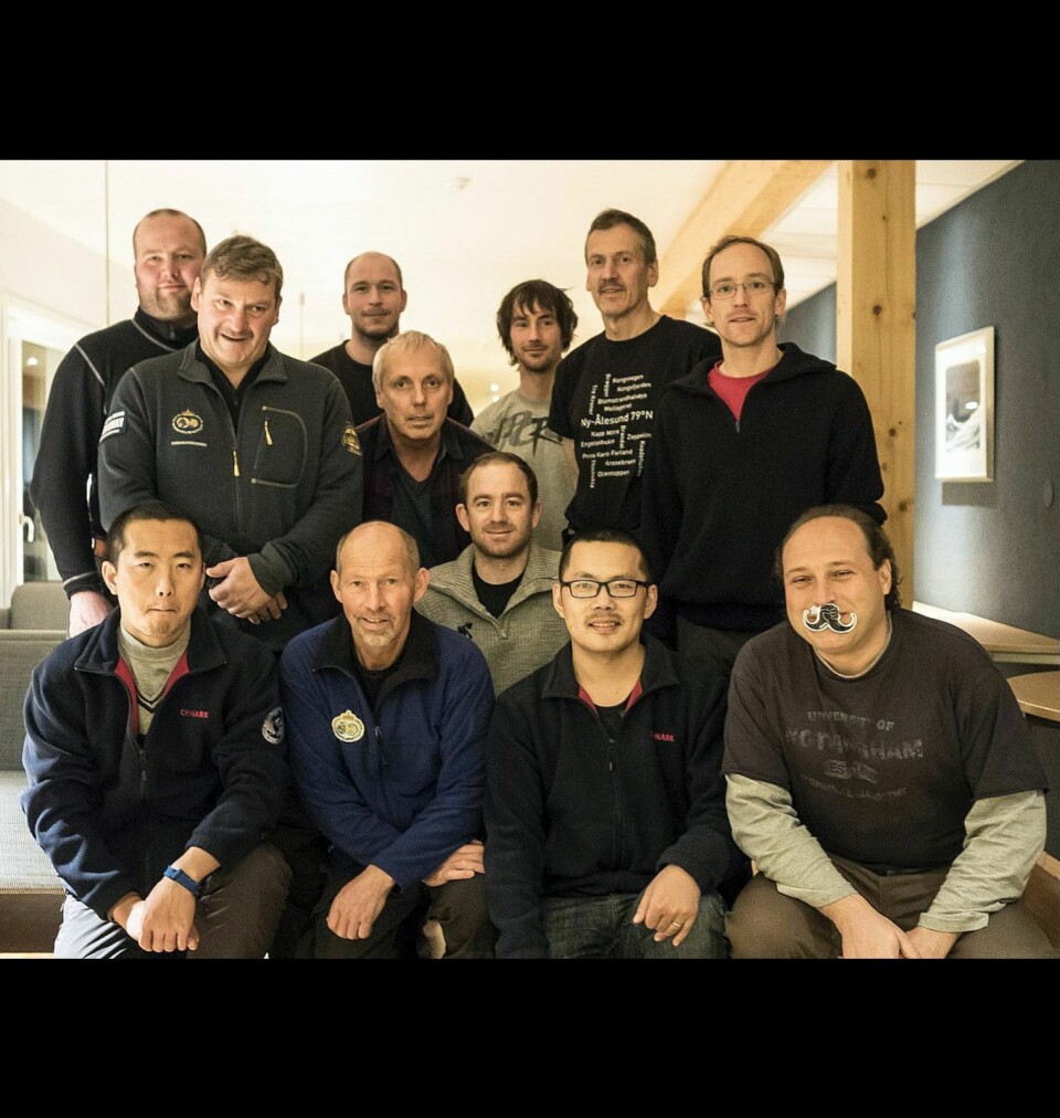 Herrer med bart: 17 av de rundt 20 som bor i Ny-Ålesund nå, er med i movember-aksjonen. Her er elleve av dem, pluss en italiener med løsbart, som har kommet til bosetningen senere. Geir Mathiassen (fremoverbøyd og nummer tre i andre rad) er svært fornøyd med oppslutningen.