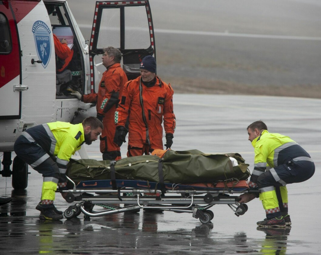 Her blir mannen fraktet på båre fra helikopteret og inn i en ventende ambulanse på Svalbard lufthavn.