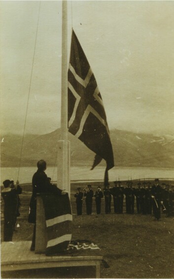 Klokken 12.00 14. august 1925 ble det norske splittflagg heist og Svalbard var en del av Norge. Justisminister Paal Berg følger med fra talerstolen, marinemusikerne blåser fanfare og æreskompaniet presenterer geværer.