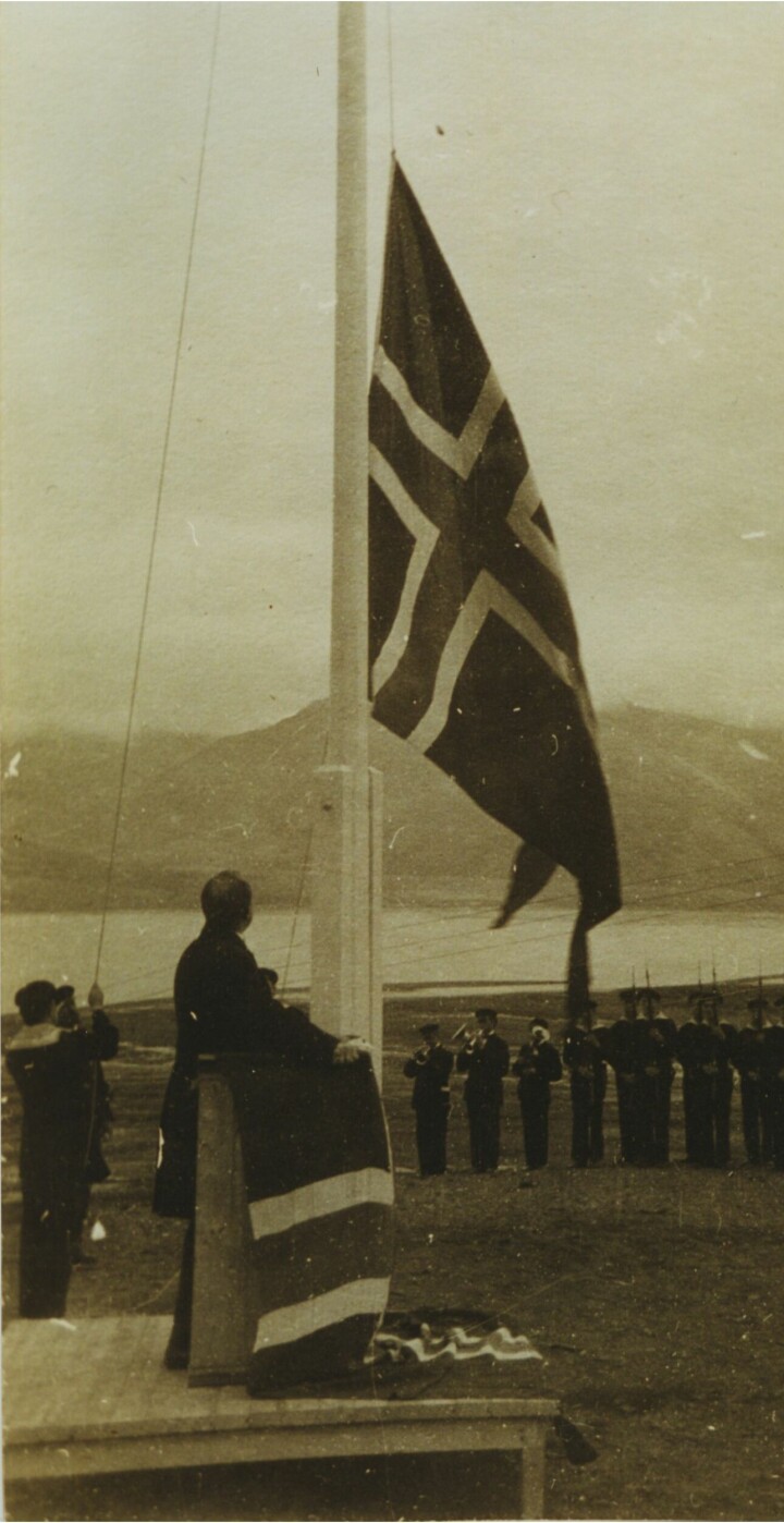 Klokken 12.00 14. august 1925 ble det norske splittflagg heist og Svalbard var en del av Norge. Justisminister Paal Berg følger med fra talerstolen, marinemusikerne blåser fanfare og æreskompaniet presenterer geværer.