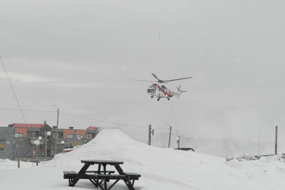 Et helikopter lander like ved Longyearbyen sykehus i tett snødrev.